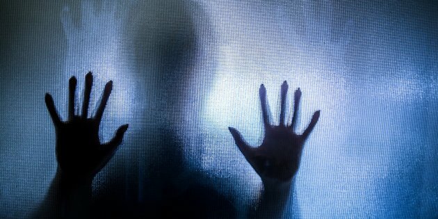 Spooky silhouette of woman with hands pressed against glass window